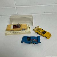 Three Solido diecast cars: yellow Ford T-Bird on base with cover, yellow race car, blue Alpine Renault