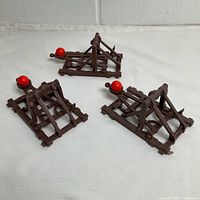 Three brown plastic catapults with red balls displayed on white surface