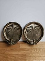 Front view of both brass shell sconces showing candle cups and patina