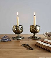 Pair of brass goblet candle holders with tapers lit, showing overall look and scale