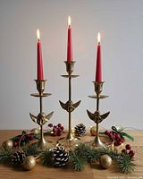 Three brass candlestick holders with red candles and holiday props displayed