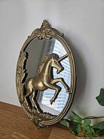 Front angled view showing oval brass frame, unicorn figure, mirrored glass