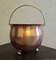 Front view showing copper body, brass handle, three brass ball feet