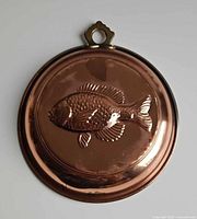 Front of copper mold showing embossed fish and brass loop