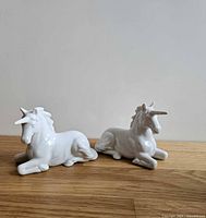 Both white porcelain unicorn figurines side by side on wood surface