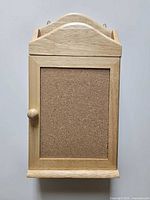 Front view of closed wooden key cabinet showing corkboard panel and arched top mail slot