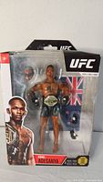 Front of sealed UFC Israel Adesanya action figure showing figure, belt, extra hands, flag backdrop