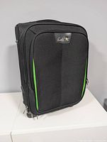 Front view of Caribbean Joe carry-on showing black fabric, green trim, front zip pocket, logo badge