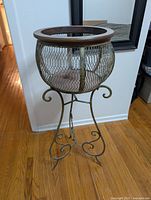 Full view of plant stand showing metal scroll legs, mesh basket, and wood rim