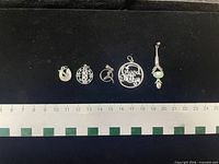 Front view of six sterling charms and pendants aligned with ruler for scale