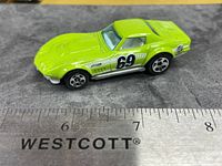 Left side view of lime green Hot Wheels ‘69 COPO Corvette with number 69 graphic, ruler for scale