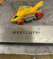 Left side profile showing yellow body, flame graphics, chrome engine, red wheels with ruler for scale