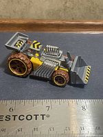 Left side view of Hot Wheels loader car showing yellow/grey body, brown wheels, bucket, hazard stripes