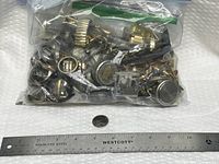 Full view of sealed plastic bag filled with assorted watch parts beside ruler and coin for scale