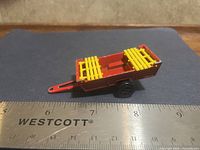 Side view showing red body, yellow gate, black wheel, ruler for scale