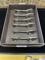 Six dog-shaped knife rests in box, side view