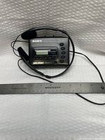 Front view showing Sony Walkman FM/AM radio with headphones and ruler for scale