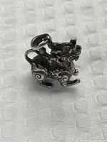 Front view of sterling silver mythical creature charm showing ruby eyes and scrollwork