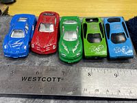 Top view of five toy cars aligned beside ruler for scale
