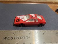 Side view of red die-cast Lotus-style coupe beside ruler