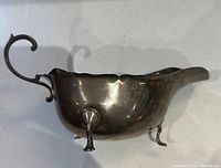 Side profile of the sterling silver creamer showing three feet, handle and spout