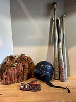 Group shot of all baseball items: four bats, three gloves, helmet, batting gloves