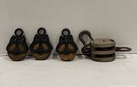 Four antique wooden pulleys aligned; three single-sheave units with cast iron cheeks and one double-sheave unit with hook.