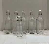 Six clear glass IKEA swing-top bottles, five tall and one shorter, with white stoppers