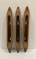 Front view of three wooden weaving shuttles standing upright, showing hollow bobbin cavities