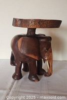 Front view of carved wooden elephant table showing tusks, trunk, circular top