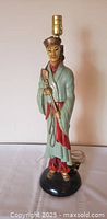 Front view of chalkware Asian man figural lamp showing colors, pose, socket, cord