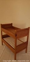 Front angled view of two-tier wooden doll bunk bed showing light wood frame and both bunks