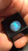 Round Ethiopian opal cabochon in display case showing blue and green play of colour