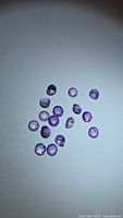 Group of 15 small round purple amethyst gems on flat surface