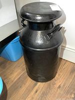 Full view of black painted metal milk can with lid and handles