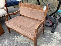 Front view of solid wood bench showing carved crest rail, arms, legs and brown upholstery
