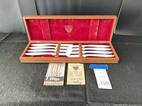 Open wooden case showing 8 steak knives in red interior with paperwork displayed in front