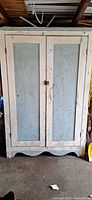 Front view of distressed white and blue wooden cabinet with two doors and scalloped base