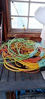 Pile of coiled green, yellow and orange heavy-duty extension cords on table