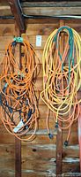Two groups of coiled orange and yellow outdoor extension cords hanging on wall studs