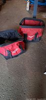 Two Milwaukee red and black soft-sided tool bags on floor