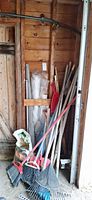 Group of long-handled tools leaning in shed corner