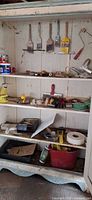Cupboard with shelves showing brushes, roller frame, paint cans, tape, putty knife, plastic bin