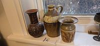 Three pottery pieces on windowsill: jug, floral vase, flower frog vase