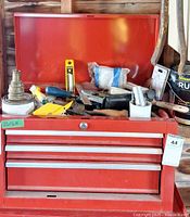 Front view showing open lid, drawers, lock cylinder, red finish