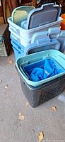 Stacked large blue totes with grey lids next to black hamper-style bin