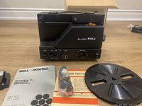 Projector, reel, manuals, microphone, cables, and open box displayed on floor