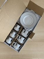 Open box showing six cups individually separated and stack of saucers