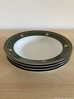 Stack of four Trisa porcelain soup plates showing green and gold rims
