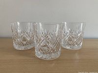 Three matching cut glass whiskey tumblers on wood surface